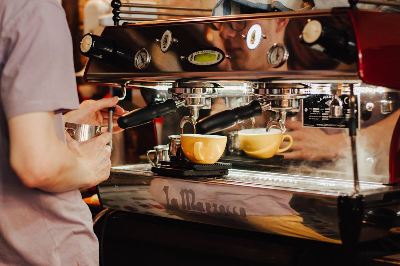 Barista using espresso machine to brew coffee in a café, showcasing coffee preparation process.