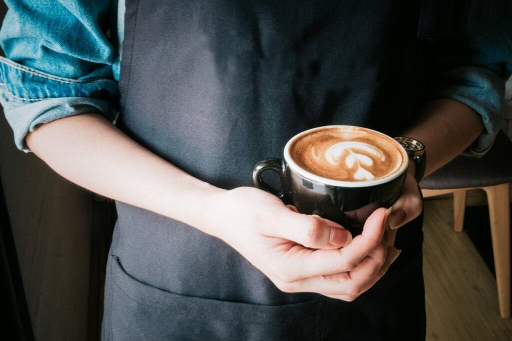 A barista holds a coffee cup with beautiful latte art in a cozy café setting.